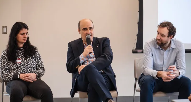 Three panelists seated in front of the audience, one speaking into a microphone